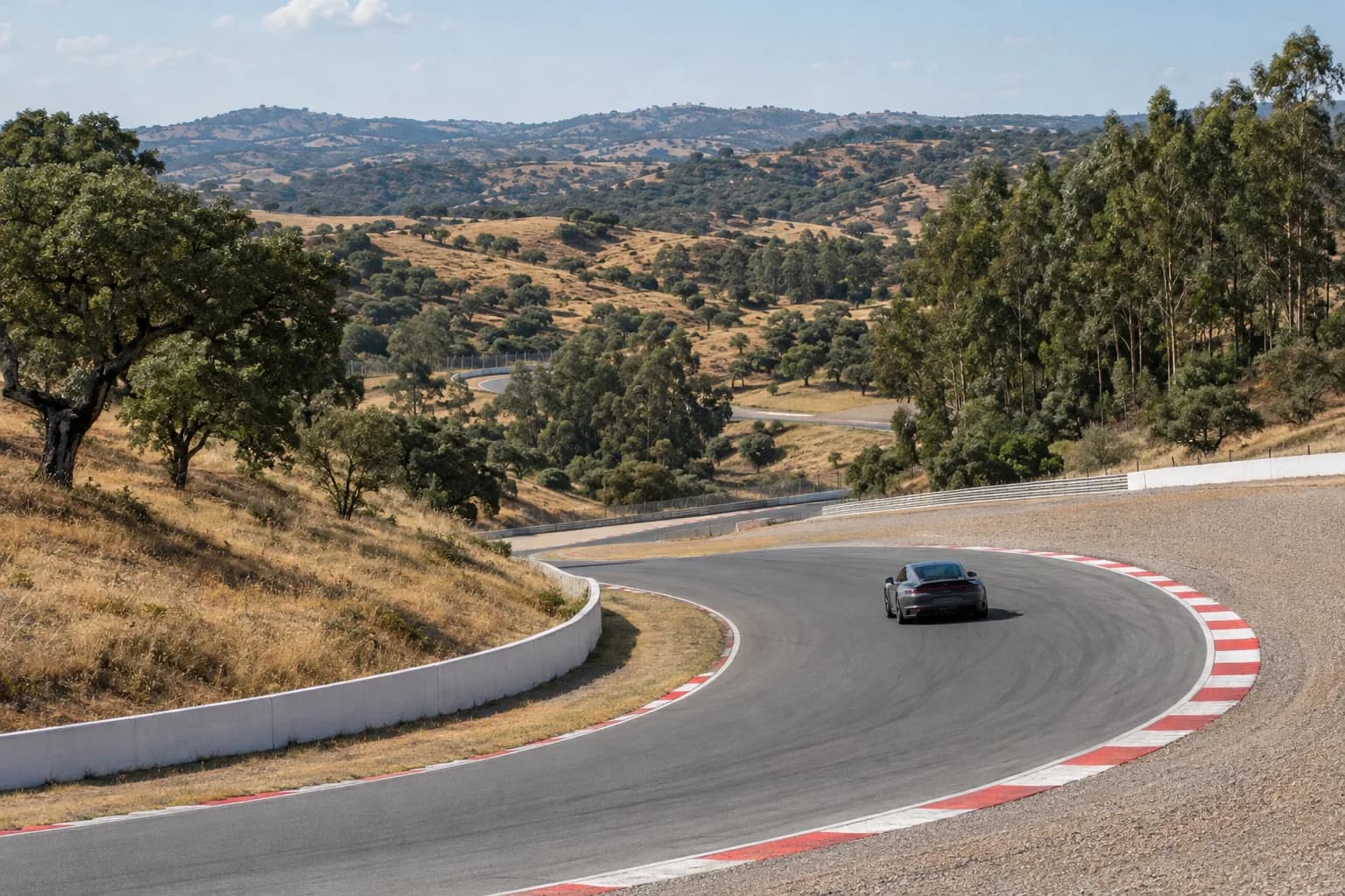 An empty motor-racing circuit bend in rolling hills with a single grey sports car